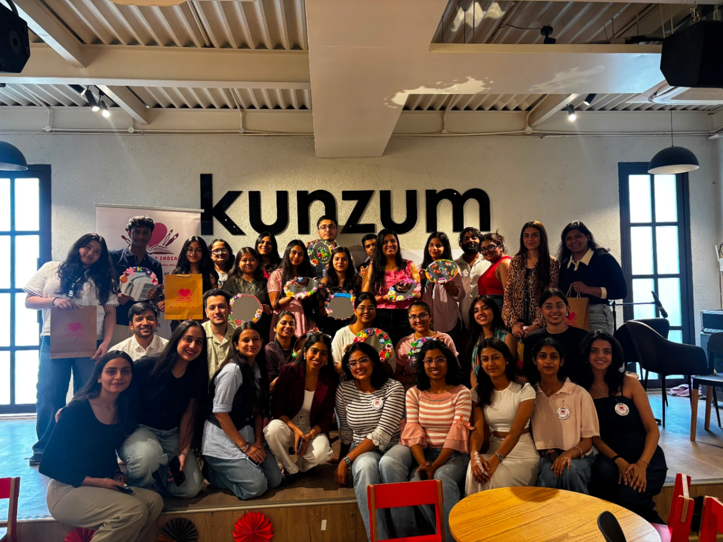 A large group of workshop participants on a low stage, holding up the mirrors and embroidery hoops they decorated.