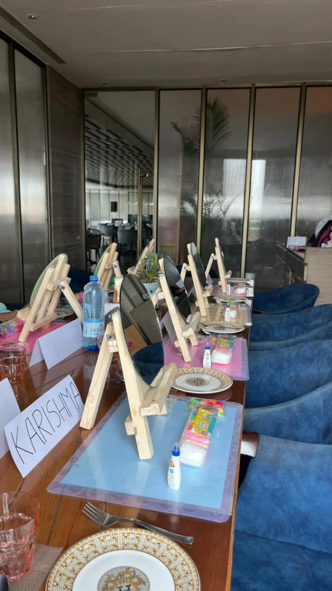 A long table laid out for a private art session, with a wooden easel, a mirror, clay and a named place card at every seat.